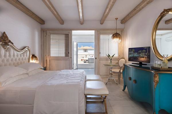 Innenansicht des Schlafzimmers im Mitsis Laguna Resort mit großem Bett, blauem Sideboard und offenem Balkon