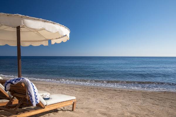Strand des Mitsis Laguna Resorts mit zwei Sonnenliegen unter einem Sonnenschirm am Meer