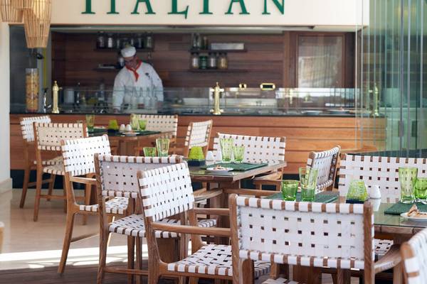 Innenansicht des italienischen Restaurants des Mitsis Laguna Resorts mit Tischen, Stühlen und einem Koch hinter der Theke.