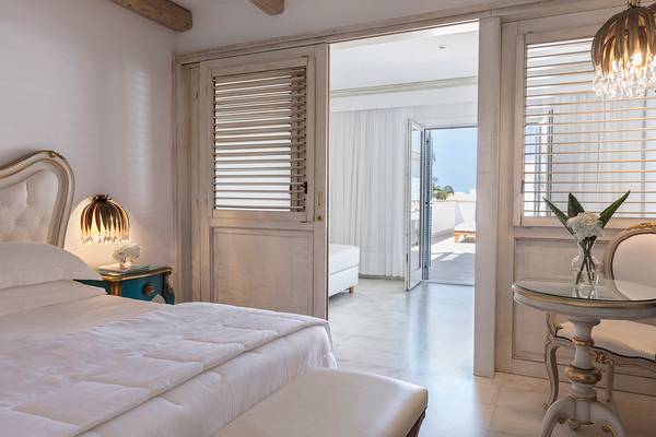 Innenansicht des Schlafzimmers im Mitsis Laguna Resort mit Bett, Nachttisch, Lampe und offenem Balkon.