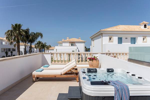 Balkon des Mitsis Laguna Resorts mit Whirlpool und Liegen vor einem Gebäude mit blauem Himmel