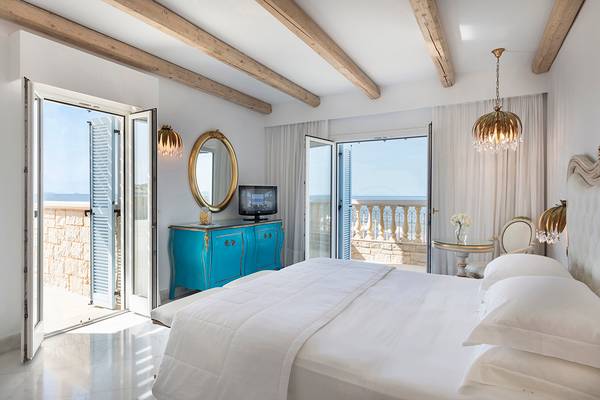 Schlafzimmer im Mitsis Laguna Resort mit Blick auf das Meer, blauem Möbelstück und offenem Balkon.