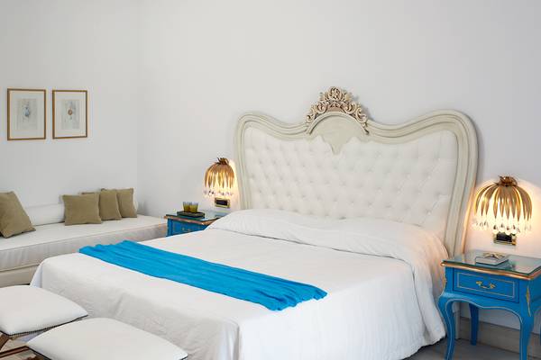Schlafzimmer im Mitsis Laguna Resort mit weißem Bett, blauer Decke und dekorativen Nachttischen.