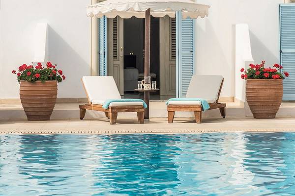 Zwei Lounge-Sessel unter einem Schirm neben einem Pool am Mitsis Laguna Resort.