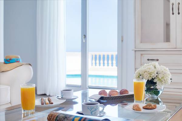 Frühstückstisch im Mitsis Laguna Resort mit Getränken und Gebäck auf einem Glastisch.