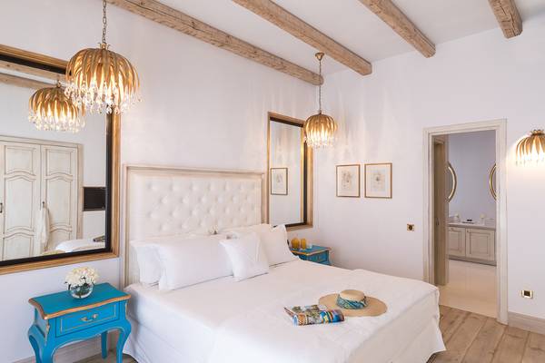 Schlafzimmer im Mitsis Laguna Resort mit weißem Bett, blauen Nachttischen und Kristalllampen.