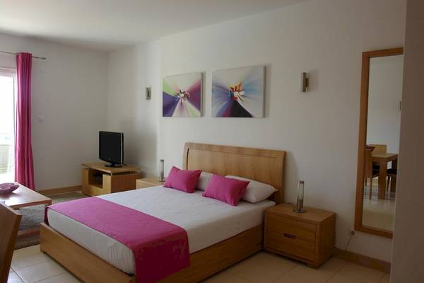 Schlafzimmer im Agua Hotels Sal Vila Verde mit einem großen Bett, Fernseher, Nachttischen und Gemälden an der Wand.