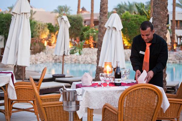 Ein Kellner bereitet einen Tisch im Freien im Ghazala Gardens Hotel vor.