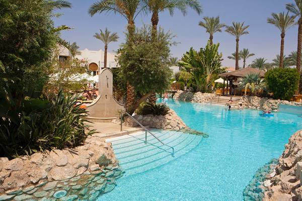 Ein blauer Pool im Ghazala Gardens Hotel mit Palmen und Felsen im Hintergrund.