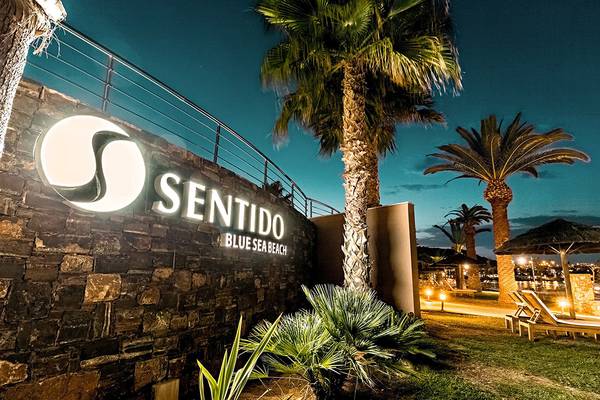 Das Eingangsschild des Sentido Blue Sea Beach Hotels bei Nacht, mit Beleuchtung und Palmen im Vordergrund.