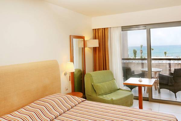 Hotelzimmer im Blue Sea Beach Hotel mit Meerblick, Bett, Spiegel, Sessel und Balkonmöbeln.