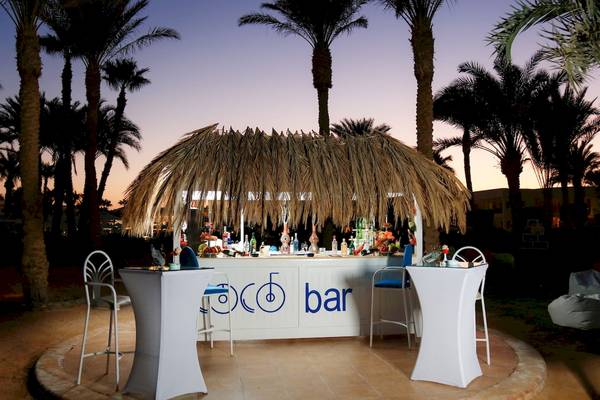 Außenbereich des LABRANDA Royal Makadi Hotels mit Bar, umgeben von Palmen, bei Sonnenuntergang.