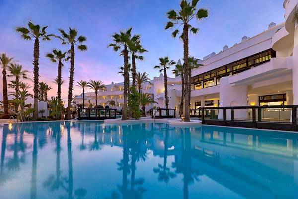 Außenpool des H10 Estepona Palace Hotels mit Palmen und weißem Gebäude im Hintergrund
