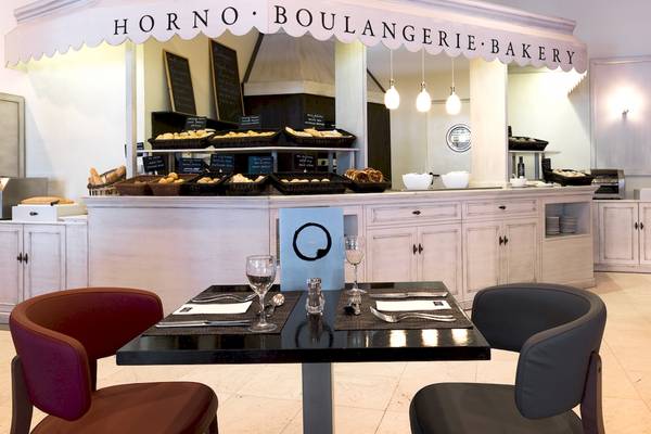 Innenansicht der Bäckerei und des Cafés im H10 Estepona Palace mit Tischen und Stühlen.