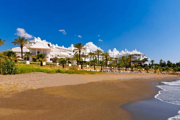 Außenansicht des H10 Estepona Palace Hotels mit Blick auf eine lange, helle Sandstrand und das Meer.