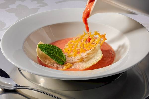 Ein Gericht mit Tomatensuppe in einer weißen Schüssel, serviert mit Minze und geriebenem Käse.