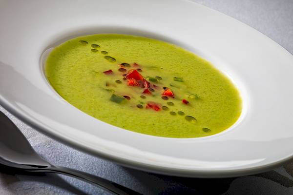 Grüne Suppe in einem weißen Teller mit roten Paprikaschoten und grünem Blatt.