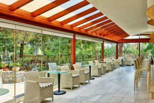 Innenbereich der Terrasse im Apollonia Beach Resort & Spa mit Tischen, Stühlen und Pflanzen.