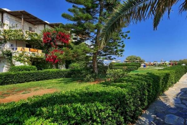 Außenbereich des Apollonia Beach Resort & Spa mit Gehweg, Büschen und Bäumen.