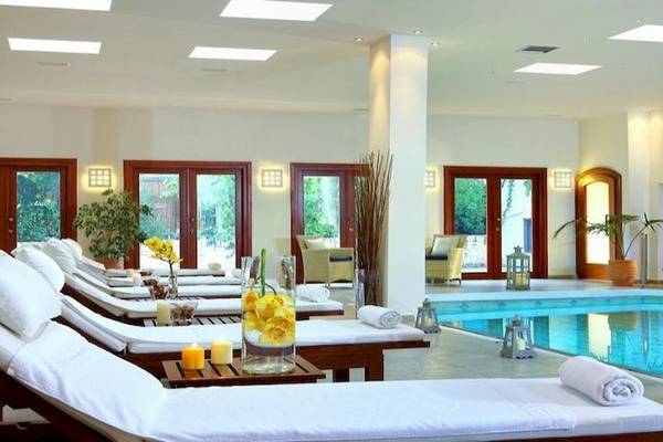 Innenpoolbereich des Apollonia Beach Resort & Spa mit weißen Liegen und Pflanzen.