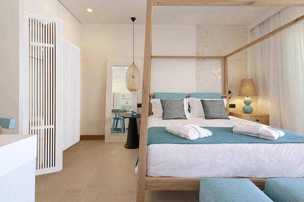 Schlafzimmer im Domes Noruz Chania Hotel mit Himmelbett, blauen Kissen und weißen Decken.