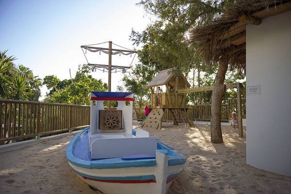 Ein Kinderspielplatz mit einem Boot, Sandkasten, Rutsche und Baumhaus.