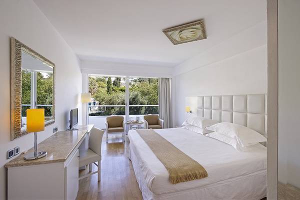 Innenansicht eines Zimmers im Grecian Sands Hotel mit Doppelbett, Schreibtisch und Balkon.