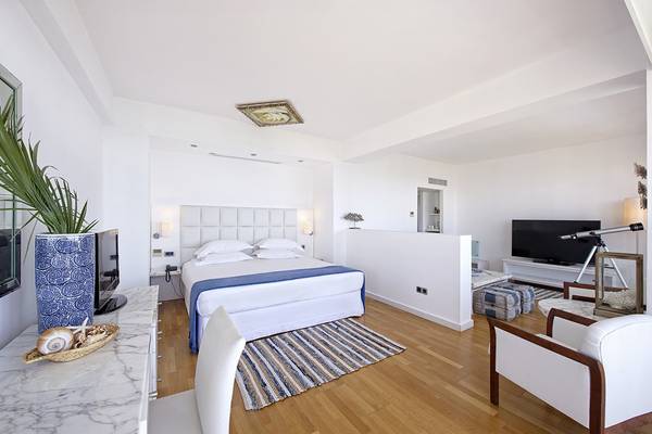 Das elegante Schlafzimmer des Grecian Sands Hotels mit weißem Bett, blauer Bettwäsche und modernen Möbeln.