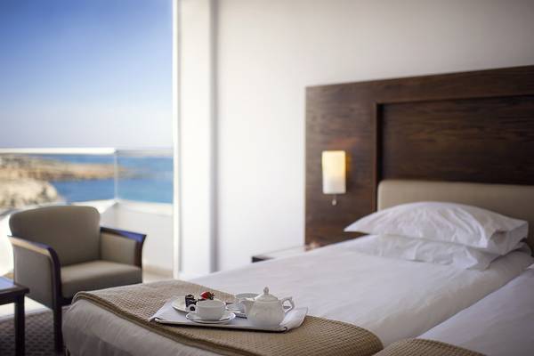 Doppelzimmer im Grecian Sands Hotel mit Meerblick, mit einem Bett, einem Tisch und einem Stuhl.