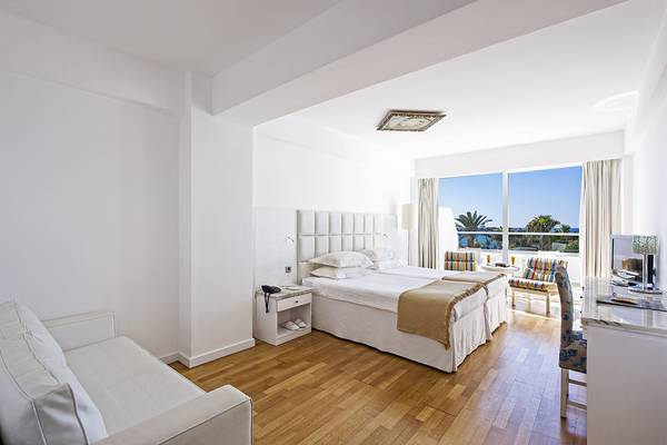 Innenansicht eines Zimmers im Grecian Sands Hotel mit großem Bett, Wohnzimmersofa und Blick auf das Meer.