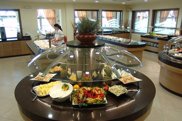 Buffet-Tisch im Europa Beach Hotel mit verschiedenen Gerichten und einer Angestellten im Hintergrund.