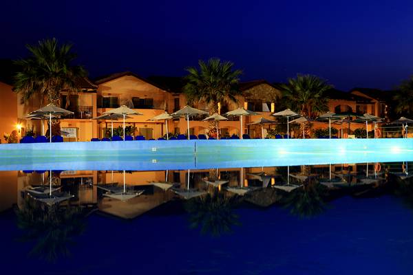 Ein großer Swimmingpool mit reflektierten Sonnenschirmen und Gebäuden im Hintergrund bei Nacht im LABRANDA Marine Aquapark.