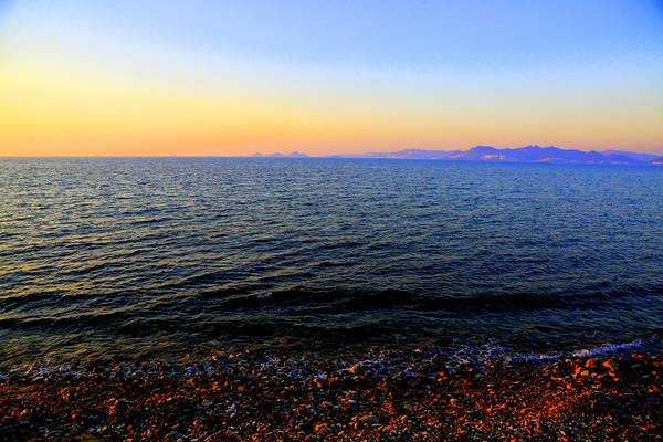 Abendlicher Meerblick mit Felsstrand und ruhigen Wellen am Horizont