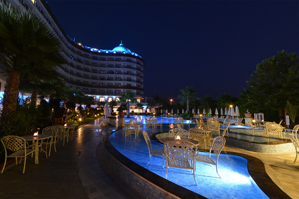 Der Poolbereich des Dream World Aqua Hotels ist nachts mit blauen Lichtern beleuchtet und bietet einen Blick auf das Hotelgebäude, einen Swimmingpool und gesellige Tische und Stühle.