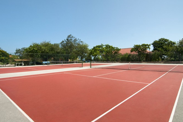 Tennisplatz im Hotel Dreams Curacao Resort, Spa & Casino mit roten Belägen und grünen Bäumen im Hintergrund.
