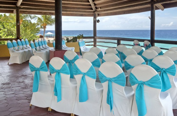 Hochzeitszeremonie im Freiluft-Resort mit Blick auf das Meer, mit weißen Stühlen und blauen Schleifen.
