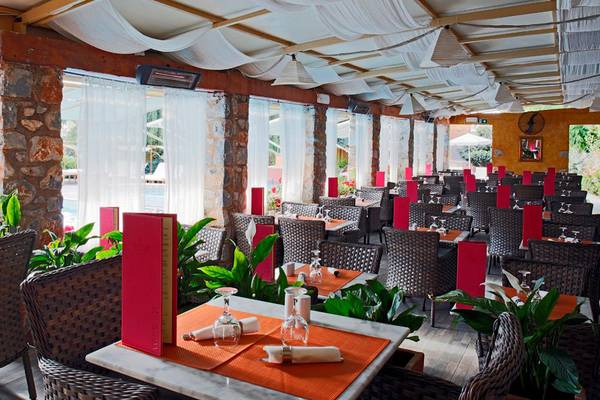 Innenansicht des Restaurants im Orpheas Resort mit weißen Vorhängen und roten Tischkarten.