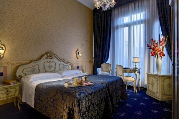 Doppelbett-Zimmer im Hotel Montecarlo mit blauem Teppich und weißen Vorhängen.
