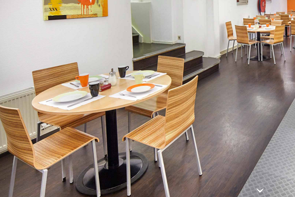 Frühstücksraum im Nova Hotel mit Tischen, Stühlen und Frühstücksbuffet.