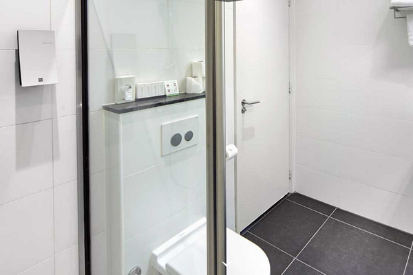 Das Badezimmer im Nova Hotel mit einer Dusche, Toilette, Waschbecken und Fliesenboden.