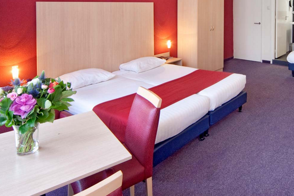 Innenansicht eines Doppelzimmers im Nova Hotel mit zwei Betten, einem Tisch und einem Blumenstrauß.