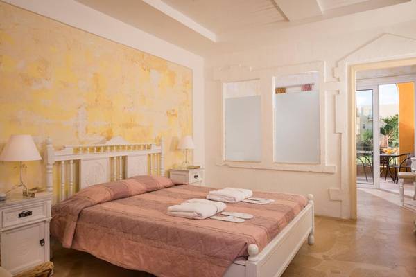 Schlafzimmer im Orpheas Resort mit gelben Wänden, einem Bett, Nachttischen und einem Balkon.