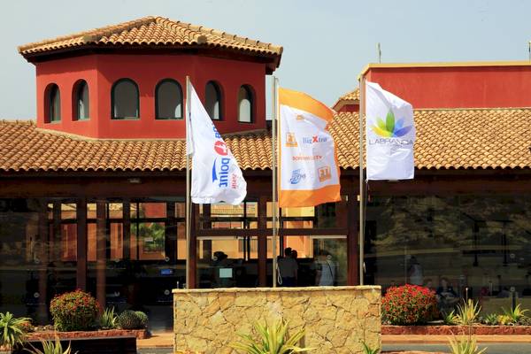 Eingang des Bluesea Aloe Corralejo Hotels mit bunten Flaggen und Gebäuden im Hintergrund.