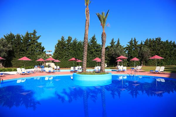 Ein blauer Pool im Blue Bay Beach Resort mit Sonnenliegen und roten Sonnenschirmen.