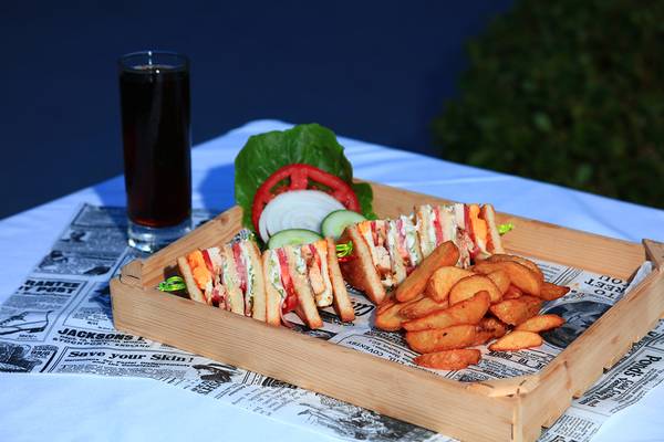 Eine Holzschale mit Sandwiches und Pommes auf einer Zeitung auf einem Tisch.