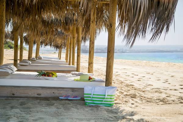 Liegestuhl am Strand des Asterias Beach Hotels mit Strohdach und Früchtekorb.
