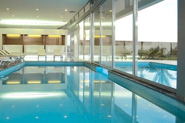 Innenpool im Crystal Centro Resort mit weißen Liegen und großen Glaswänden.
