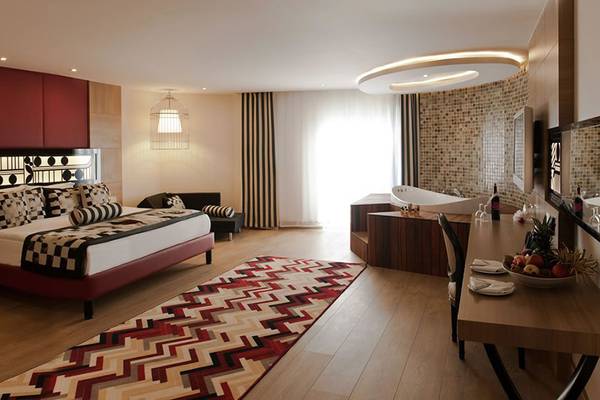 Innenansicht eines Zimmers im Delphin Imperial Hotel mit einem großen Bett, einem Esstisch und einem Badezimmer mit Badewanne.
