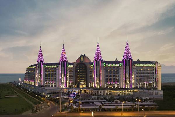 Das Delphin Imperial Hotel in der Abendbeleuchtung mit violetten Lichtern und Meer im Hintergrund.