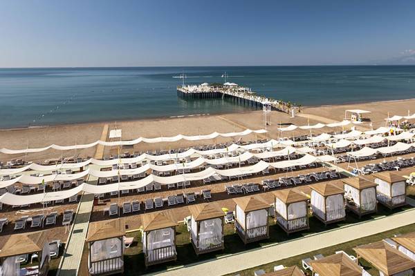Luftaufnahme des Delphin Imperial Hotels zeigt eine lange Strandlinie mit vielen weißen Sonnenschirmen und Lounge-Stuhlreihen.